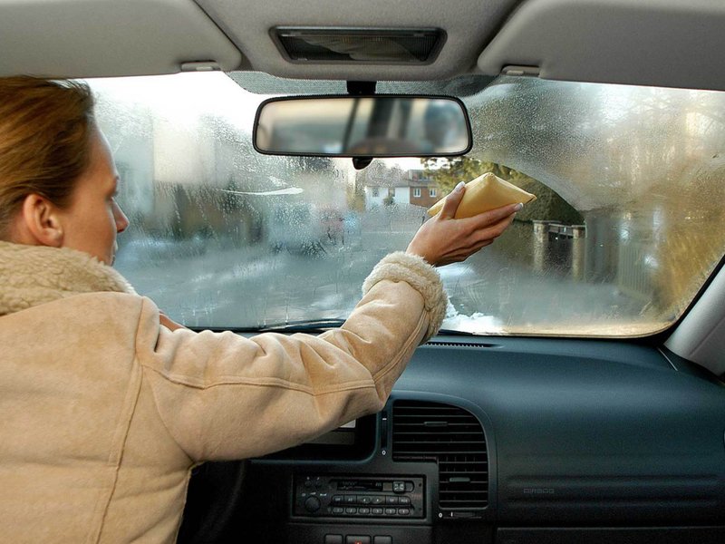 Frau macht beschlagene Windschutzscheibe im Auto von innen mit einem Schwamm frei